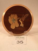 Front view of round wooden plaque with hummingbird feeding on flower in marquetry.