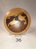 Front view of the round wooden wall plaque with marquetry killer whales depicting two orca whales in a natural wood variety against a darker wood background, mounted on clear plastic stands.