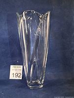 Tapered tulip-shaped Marquis by Waterford clear glass vase with four curved lobes and square base against a blue background.