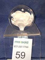 Spherical clear glass paperweight with white rose inside, displayed on a clear stand with lot number 59 sign visible in front.