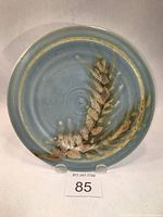 Full view of ceramic side plate showing leaf and stem design with blended glazes on sky blue background