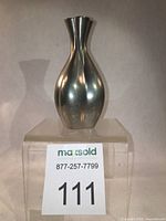 Front view of pewter vase with curved fluted design shown against white background on clear stand