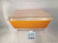 Front and top angled view of the orange rectangular Pyrex casserole dish with clear glass lid, showing shape and color.