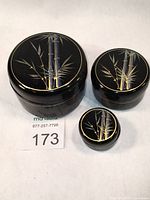 Top view showing all three black lacquered round nesting containers with gold bamboo design on lids in descending size order.