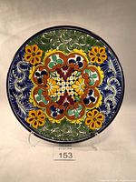 Front view of Talavera ceramic decorative plate showing detailed colorful floral and leaf patterns with yellow flowers, green leaves, and blue background.