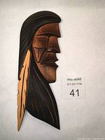 Front view of the carved wooden cedar panel showing warrior profile, painted black and natural wood stain with feather detail.