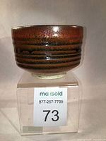 Front view of Tomaku glazed bowl showing rich brown tones and horizontal ridged texture on round form, set on acrylic stand.