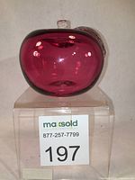 Front view of the cranberry glass apple showing the rich red color and clear glass leaf and stem on top. Smooth shiny surface is visible.