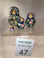 Photo showing all four vintage Matryoshka dolls arranged frontally on a transparent surface with visible MaxSold lot number.