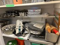 Shelf with metal bakeware including muffin tins, baking trays, disposable foil trays, rolling pins, bunt cake pan, cookie cutters, and candy molds.