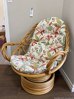Front angle of bamboo swivel chair showing twisted bamboo armrests and floral cushion
