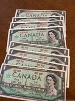 Four circulated Canadian Centennial one dollar bills arranged overlapping, showing the portrait of Queen Elizabeth II and the serial numbers, with the dates 1867-1967.