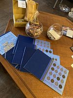 Overview of two glass bowls with loose coins, rolled coin wrappers in paper bag, and blue coin albums on wooden table