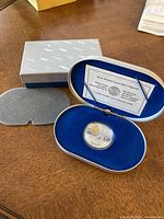 Photo showing overall lot including coin in capsule inside blue velvet-lined metal box and outer cardboard box.