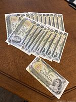 Twenty one Canadian one dollar bills laid out on a wooden surface, showing front side with portrait of Queen Elizabeth II and Canadian coat of arms visible.