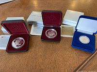 Three Canadian proof coins in original display cases with certificates on wooden surface.