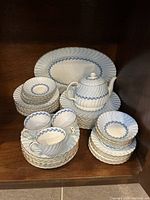 Full view of the china set stacked on shelves showing teapot, large platter, bowls, teacups, saucers, side plates, and dinner plates.
