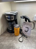 Mr. Coffee 12 cup programmable drip coffee maker, Salton cordless electric glass kettle, Braun coffee grinder all on a kitchen counter with manuals visible.