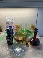 Wide photo showing entire assortment on kitchen countertop including decanters, bowls, vases, and glasses in various colors and styles.