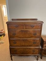 Front view of medium wood dresser showing four drawers with dark metal traditional pulls and decorative wood detailing.
