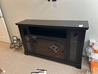 Front view of the fireplace mantel showing center electric firebox with glass door and side cupboards with glass panels.