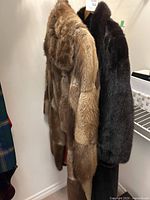 Two fur coats hung side by side: left tan & beige Eaton Fur Salon coat, right dark brown Claude Mathieu coat