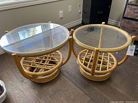 Two round bamboo occasional tables side by side on wooden floor, one larger with 24 inch diameter glass top and one smaller with 20 inch diameter glass top, both 18 inches high.