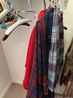Four garments hanging: two tartan kilts, one plaid wrap coat, one red pea coat.