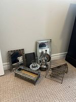 Photo showing two rectangular mirror trays, a tall black woven style napkin holder, clear glass cup with decorative metal sleeve on white glass plate, metal bowl, and vintage glass oil lamp with metal base and chimney, plus a small metal wire rack and rectangular tissue holder with floral sides.