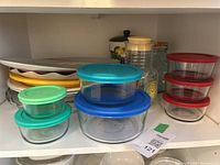 Various glass and plastic food storage containers with colorful lids, and large platters in background