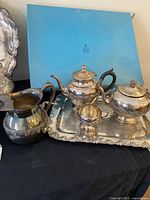 Wide view of Rogers silverplate tea set with water pitcher and ornate tray alongside Birks box