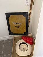 Photo of Bailey Western Hats box, cowboy hat inside, three red bandanas and wooden walking stick standing behind.