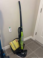 Full view of the upright Thane H2O HD steam cleaner showing the handle, base, cord wrapped on the handle, and a basket holding accessories.