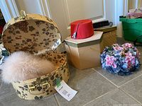 Four vintage ladies hats with three accompanying vintage-style hat boxes placed on a floor.