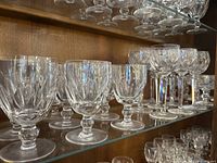 Glassware set displayed on glass shelves inside a wooden display case, showing multiple clear Waterford Crystal glasses with cut pattern designs.