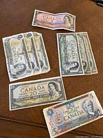 Photo of Canadian paper money including a $2 bill from 1954 (red tone), multiple $1 bills from 1954 (three visible) and 1973 (three visible), $20 bill from 1954, and $5 bill from 1979
