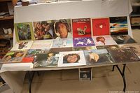 Full view of 22 vinyl albums laid out on folding table, with visible album covers of multiple artists including The Monkees and Barry Manilow.