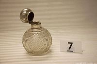 Perfume bottle upright with lid open showing cut glass body and silver top.