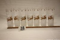 Set of seven frosted Tom Collins glasses decorated with gold and white prancing horse designs, lined up and shown from a front view with measuring tape for scale.