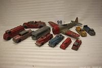 All 11 vintage metal toy vehicles arranged together, including the WWII airplane and various cars and trucks.