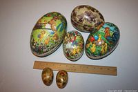 Six vintage two-piece decorated paper mache Easter eggs placed by a ruler for scale. Various sizes and colorful painted scenes including animals and flowers.