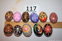 Top-down view of ten decorated Easter eggs arranged includes a ruler for scale, showing various colorful hand-painted designs and traditional motifs.