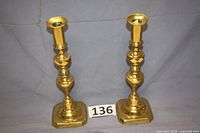 Pair of two tall solid brass candlesticks on fabric backdrop with identification number card, showing overall shape and condition.