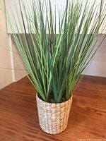 Single artificial grass plant in woven pot on wooden surface