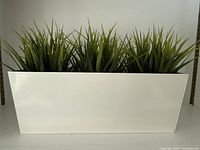 Front view of white planter containing three artificial grass plants
