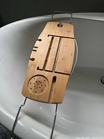 Top view of bamboo bathtub tray showing slots, wine-glass cutout, soap dish, metal arms