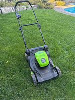 Left side view of Greenworks cordless lawn mower showing battery housing, deck, wheels and handle