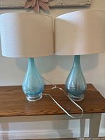 Pair of aqua glass table lamps with white shades on wood table