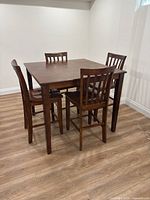 Full view of square pub-height table with four stools on wood floor