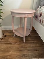 Full view of the round pink side table showing top, legs, and lower shelf